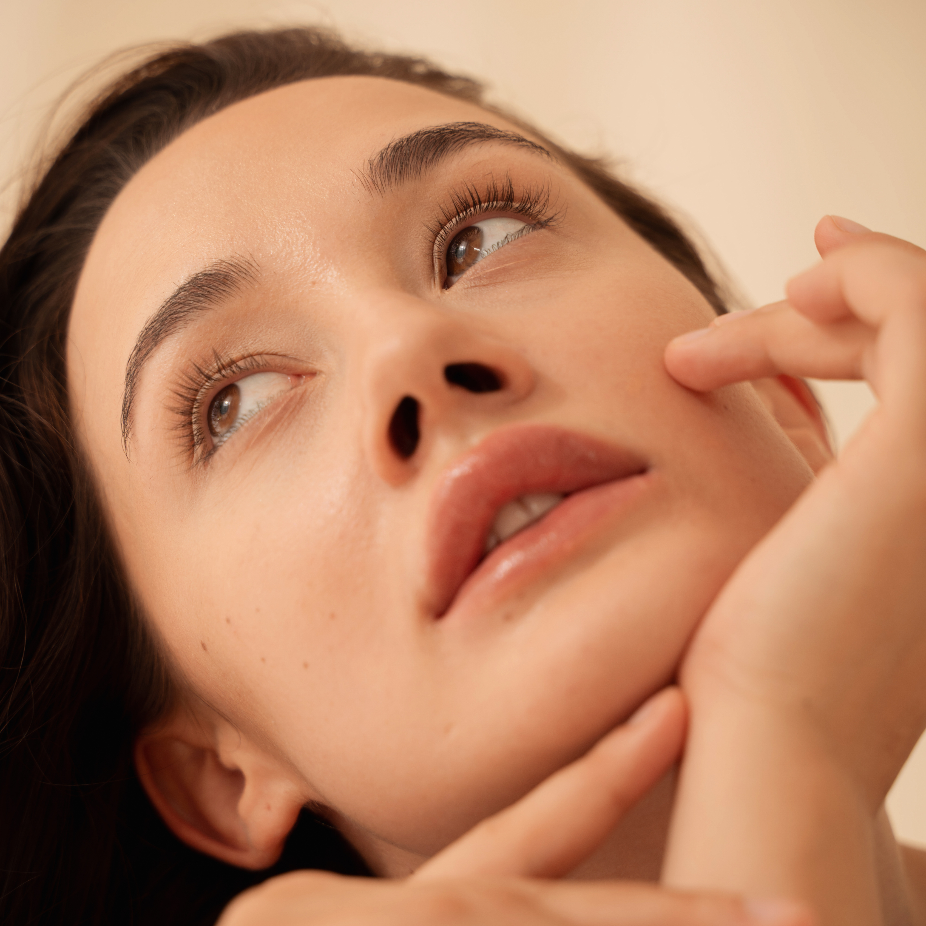 woman with plump and firm skin looking up and touching her face. Skinsetgo peptide serum for face